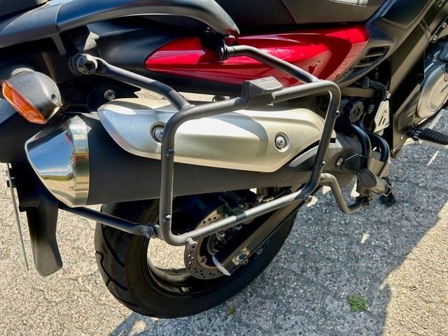 Rückansicht eines schwarz-silbernen Motorrads mit rotem Rücklicht und Gepäckträger, das auf dem Bürgersteig geparkt ist.