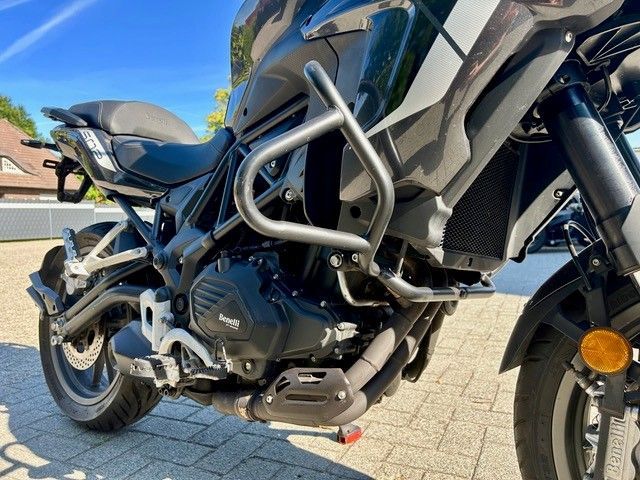 Schwarzes Adventure-Motorrad parkt auf dem Bürgersteig, Seitenansicht mit silbernen Sturzbügeln und sichtbarem Vorderrad.