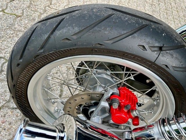 Motorrad-Hinterrad mit silbernen Speichen, rotem Bremssattel und schwarzem Reifen.