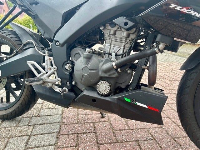 Nahaufnahme eines schwarzen Sportmotorrads mit Motor und Verkleidung sowie italienischem Flaggenaufkleber, das auf einem Backsteinpflaster geparkt ist.