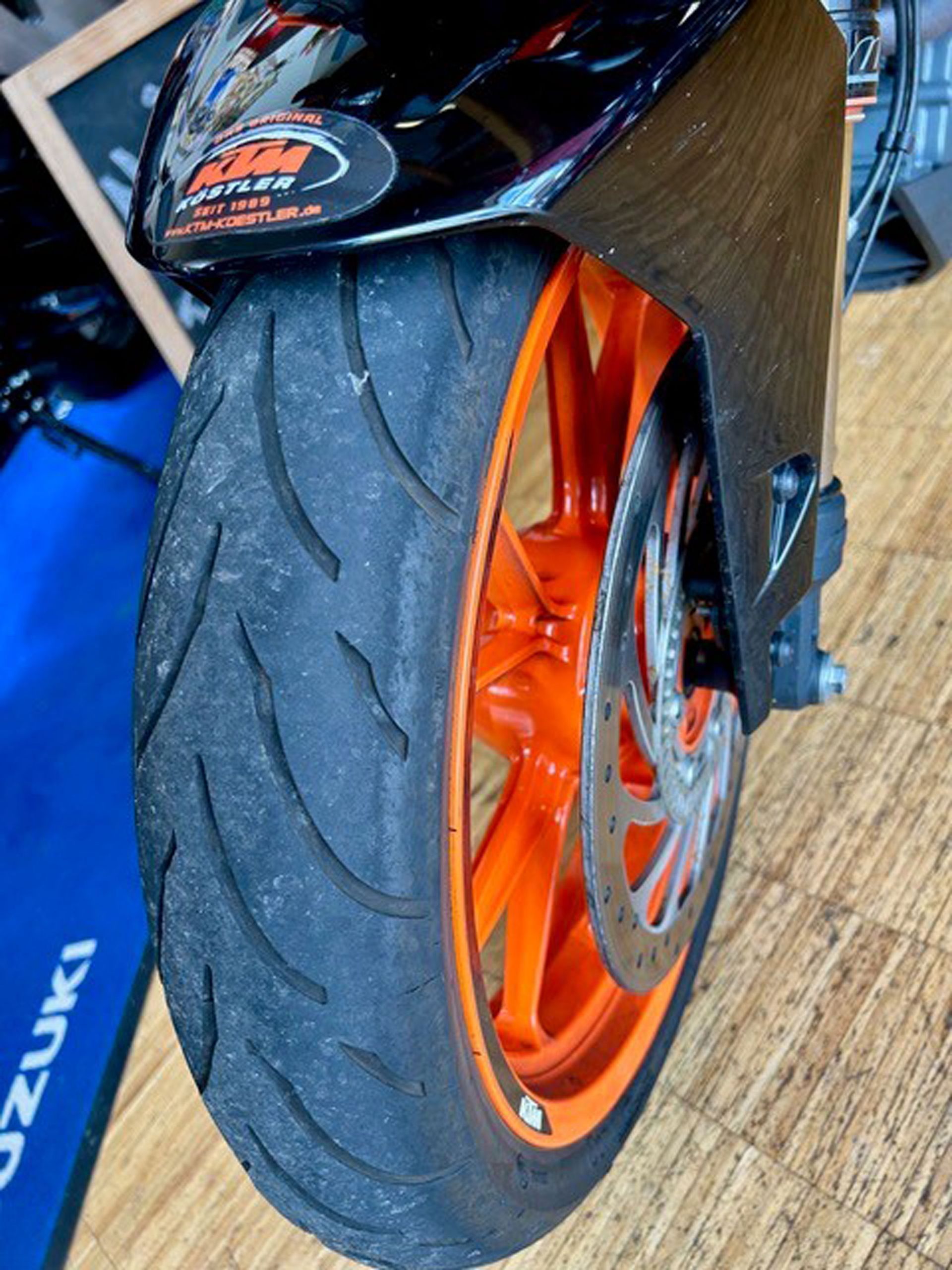 Vorderrad eines KTM-Motorrads; orangefarbene Felge und schwarzer Reifen. Der Reifen weist Abnutzungserscheinungen mit sichtbaren Rillen auf.