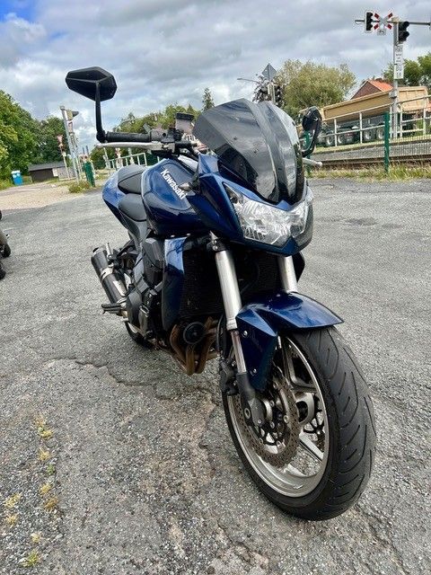 Ein blaues Sporttouring-Motorrad steht am Straßenrand und ist zur Kamera geneigt.