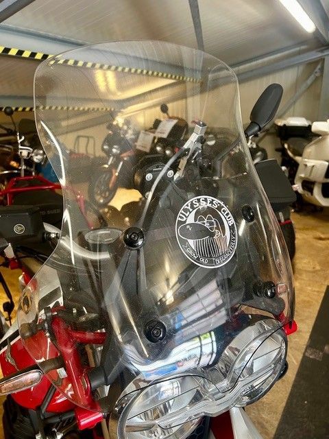 Rotes Motorrad mit klarer Windschutzscheibe und runden Scheinwerfern parkt in einer Garage.