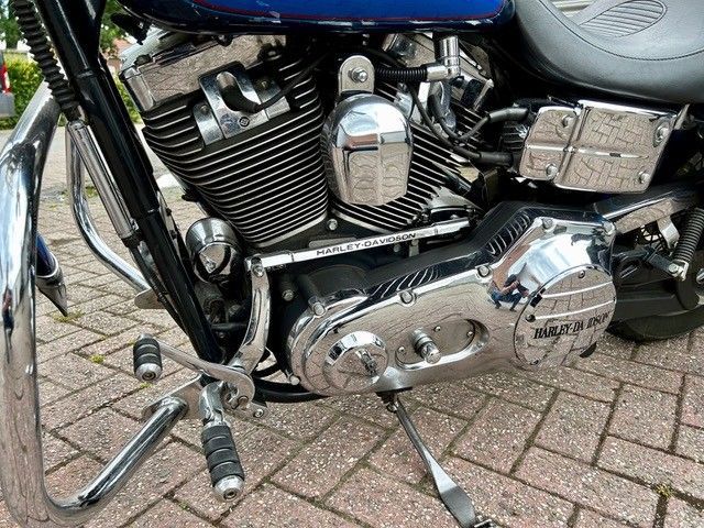 Nahaufnahme eines Harley-Davidson-Motorradmotors mit Chromdetails und blauer Farbe. Das Motorrad steht auf einer gepflasterten Fläche.