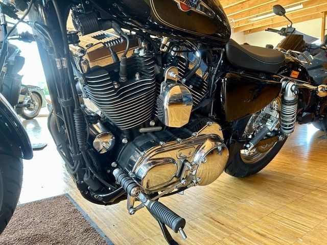 Schwarzes Cruiser-Motorrad mit verchromtem Motor und Auspuff, geparkt in einem Innenraum auf einem Holzboden.