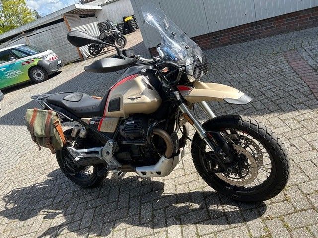 Ein Adventure-Motorrad mit Satteltaschen und Windschutzscheibe steht auf einer gepflasterten Auffahrt neben einer Garage.