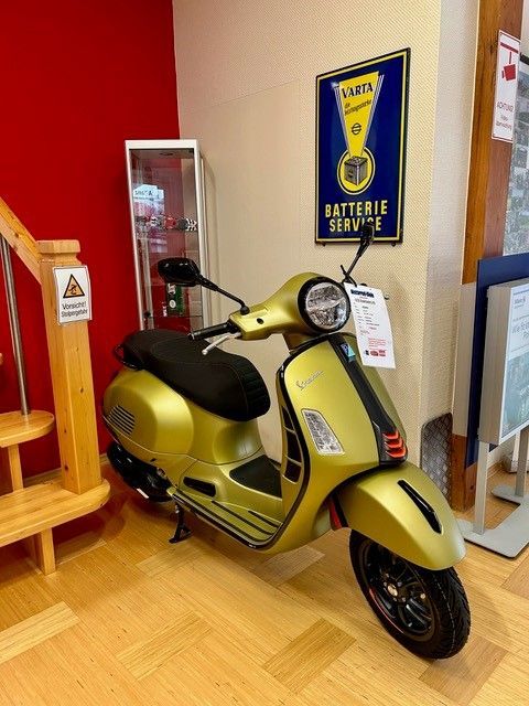 Goldener Vespa-Roller im Innenbereich, neben einer Treppe und einem Vintage-Schild.