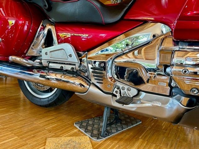 Seitenansicht eines roten und verchromten Motorrads auf Holzboden. Fußstütze sichtbar.