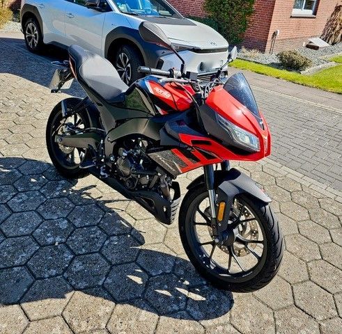 Auf einem gepflasterten Gehweg ist neben einem Auto ein rot-schwarzes Motorrad geparkt.