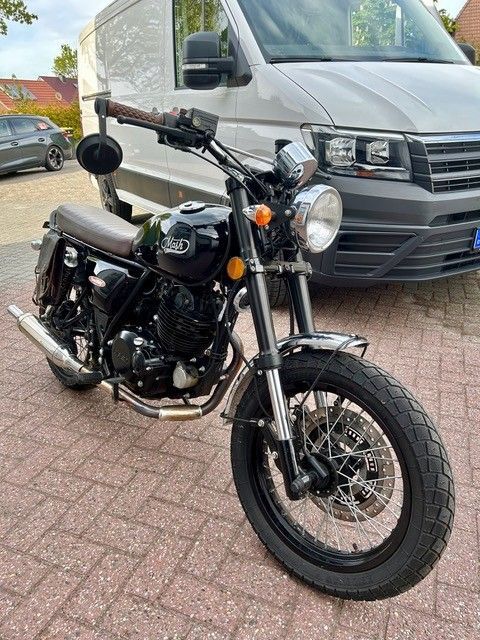 Ein schwarzes Motorrad parkte auf einer gepflasterten Auffahrt vor einem weißen Lieferwagen.