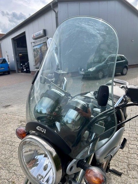 Motorrad mit hoher, klarer Windschutzscheibe, geparkt vor einer Garage