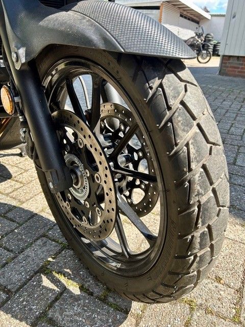 Nahaufnahme eines Motorradvorderrads mit Scheibenbremse auf einer asphaltierten Fahrbahn.