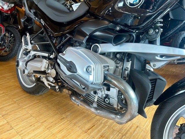 Silbernes BMW-Motorrad in einem Ausstellungsraum, Seitenansicht mit sichtbarem Motor und Auspuff auf einem Holzboden.