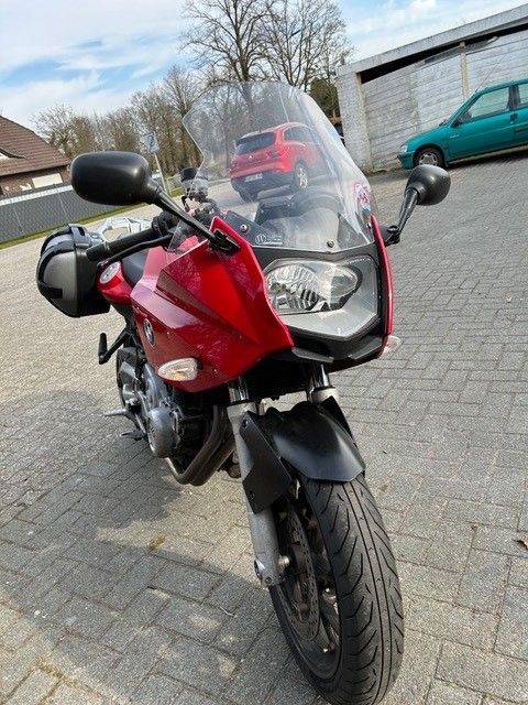 Ein rotes Motorrad mit einer klaren Windschutzscheibe steht auf einem Parkplatz