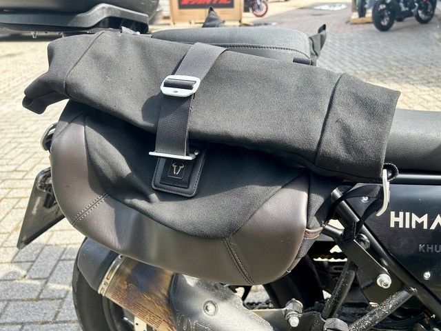 Eine schwarze Rolltasche ist auf einem Motorradsitz auf der Straße befestigt.