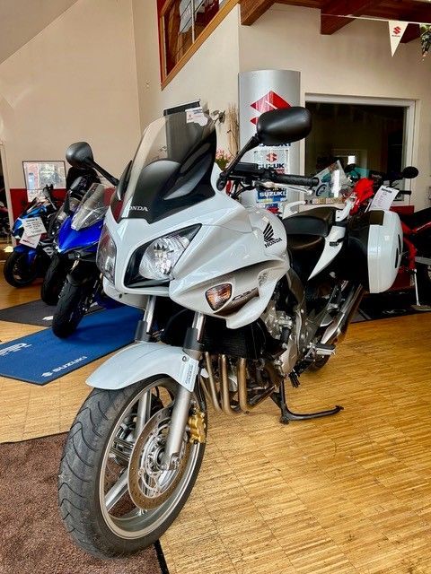 Weißes Sportmotorrad in einem Ausstellungsraum, dahinter auf einem Holzboden stehen weitere Motorräder.