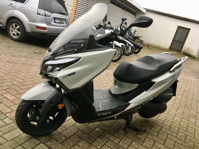 Auf einer gepflasterten Auffahrt ist neben einem Auto ein Motorroller geparkt.