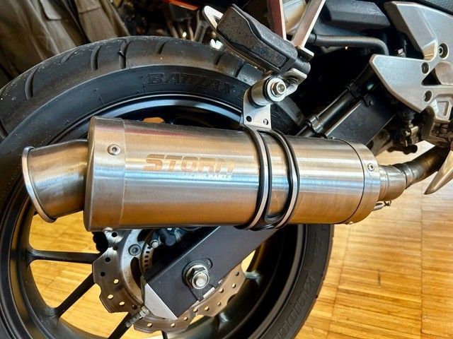 Nahaufnahme eines Motorradhinterrads mit silbernem Auspuffschalldämpfer und Endkappe aus Kohlefaser.