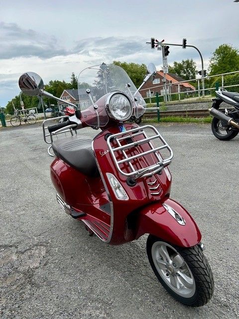 Ein roter Motorroller mit Windschutzscheibe steht auf einem Parkplatz.