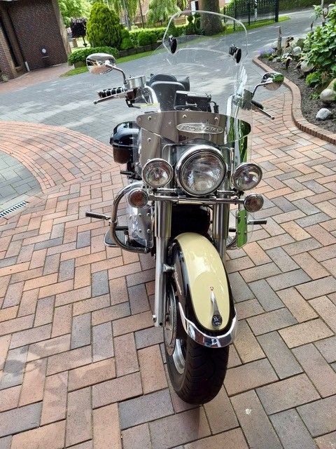 Ein verchromtes Oldtimer-Motorrad parkt auf einer gepflasterten Auffahrt, Vorderansicht mit cremefarbenem Kotflügel.