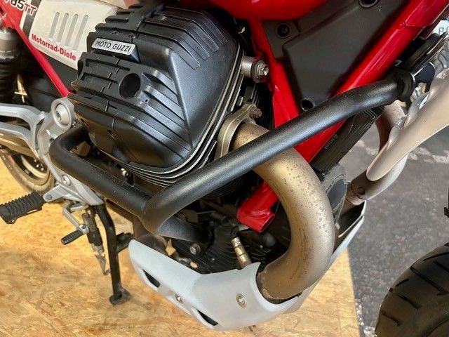 Nahaufnahme eines roten Motorradmotors mit schwarzem Auspuffrohr und silbernem Unterfahrschutz