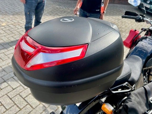 Schwarzes Motorrad-Topcase mit rotem Reflektor auf einem geparkten Motorrad im Freien