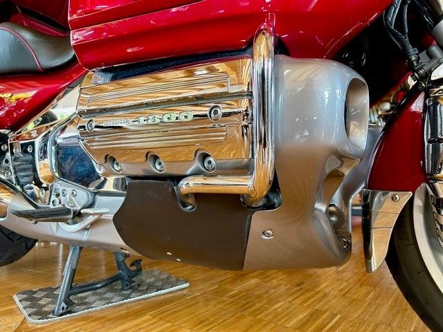 Nahaufnahme eines rot-chromfarbenen Motorradmotors mit silbernen und schwarzen Akzenten auf einem Holzboden.