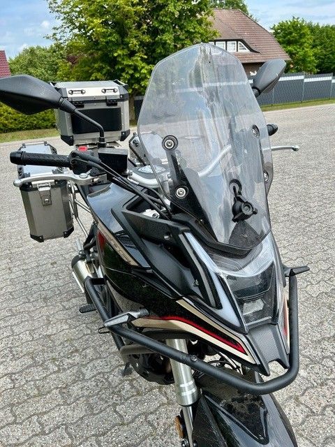 Ein schwarzes Motorrad mit einer klaren Windschutzscheibe ist auf einer gepflasterten Straße geparkt.
