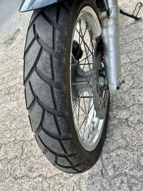 Nahaufnahme eines Motorradvorderrads mit schwarzem Profilreifen auf Asphalt.