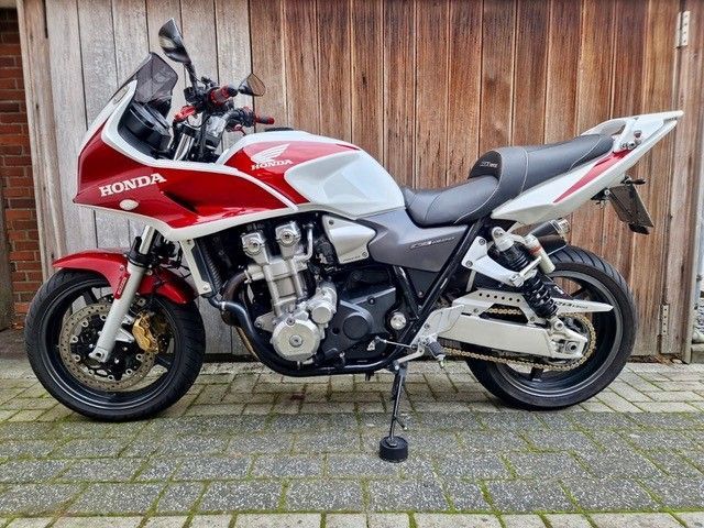 Rot-weißes Honda CB1300-Motorrad auf Pflastersteinen vor einer Holzwand geparkt.