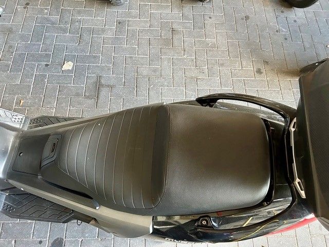Draufsicht auf einen schwarzen Roller, der auf einem gepflasterten Gehweg geparkt ist, daneben ein rotes Auto.
