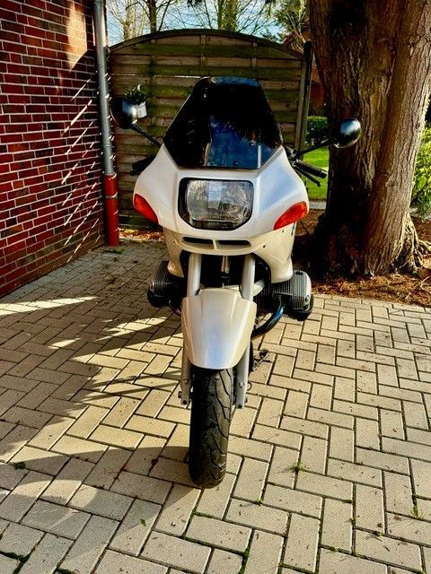 Ein weißes Motorrad ist auf einer gepflasterten Auffahrt neben einem Baum geparkt.