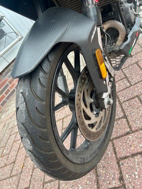 Nahaufnahme eines Motorradvorderrads mit Scheibenbremse und schwarzem Schutzblech auf Ziegelpflaster