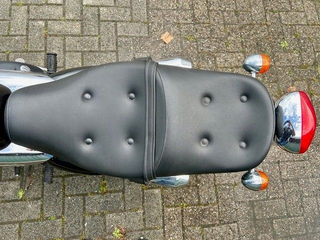Draufsicht auf einen schwarzen Motorradsitz auf Kopfsteinpflaster, rechts daneben ein rot-silberner Helm.