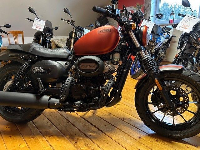 Ein rot-schwarzes Motorrad steht auf einem Holzboden in einem Ausstellungsraum.