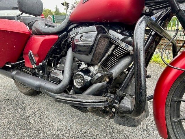 Nahaufnahme eines roten Motorrads mit schwarzem Motor und Auspuff, das im Freien auf dem Bürgersteig geparkt ist.