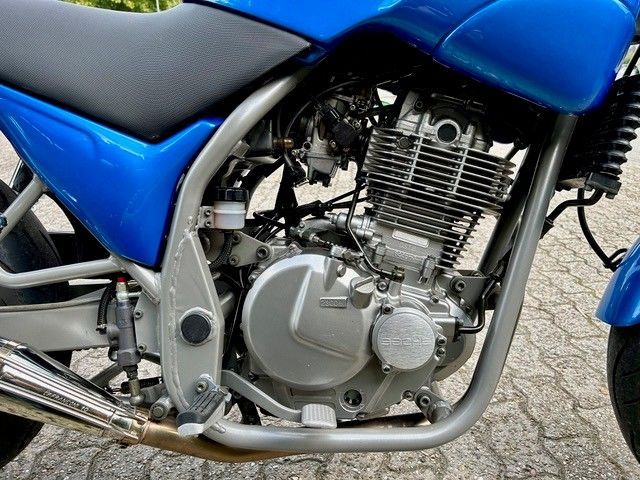 Blauer Motorradmotor, Seitenansicht, silberner Rahmen und Auspuff, Asphalthintergrund.