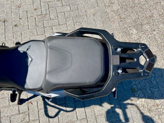 Draufsicht auf einen Rollersitz und Gepäckträger, die auf einer gepflasterten Fläche im Sonnenlicht geparkt sind.