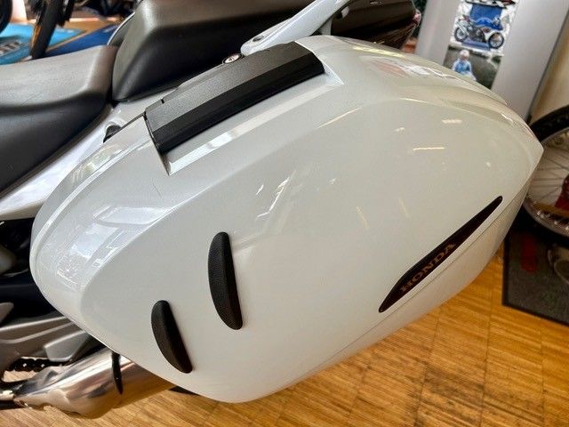 Weißer Motorrad-Hartschalenkoffer mit schwarzen Lüftungsschlitzen, der auf einem Holzboden in einem Geschäft steht.