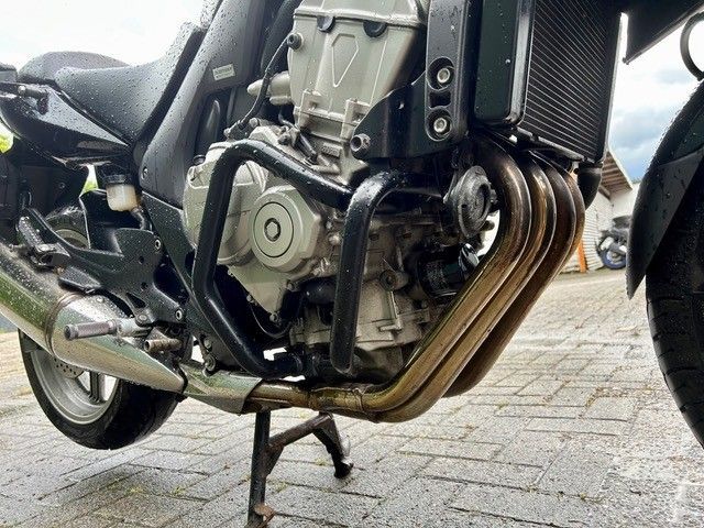 Nahaufnahme eines schwarzen Motorradmotors mit goldenen Auspuffrohren, der im Freien auf einem Hauptständer steht.
