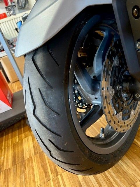 Nahaufnahme eines Motorradvorderrads mit Scheibenbremse auf einem Holzboden in einem Innenraum