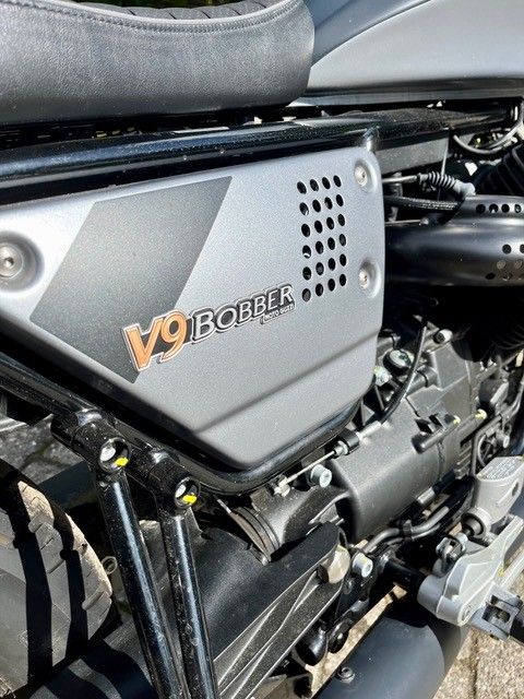 Nahaufnahme der Seitenverkleidung eines V9-Bobber-Motorrads in Silber und Schwarz mit orangefarbener Beschriftung.