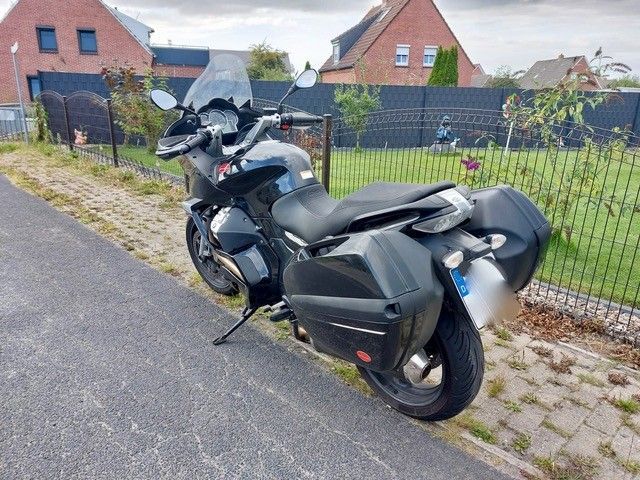 Schwarzes Moto Guzzi-Tourenmotorrad mit harten Seitenkoffern und getönter Windschutzscheibe, am Straßenrand geparkt.