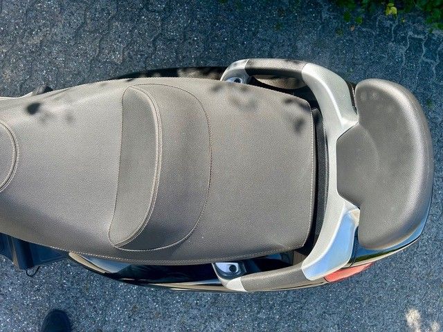 Draufsicht auf einen grauen Rollersitz und Gepäckträger auf dunklem Asphalt