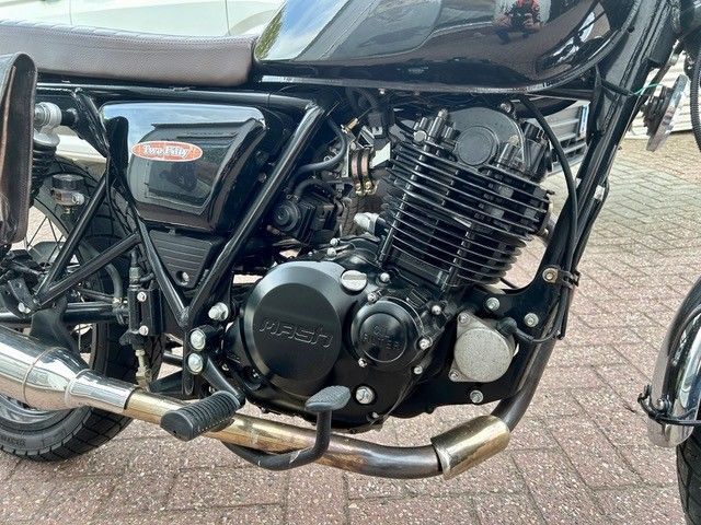 Schwarzes Custom-Motorrad mit freiliegendem Motor, verchromten Auspuffrohren und einem dreieckigen Luftfilter an der Seite.