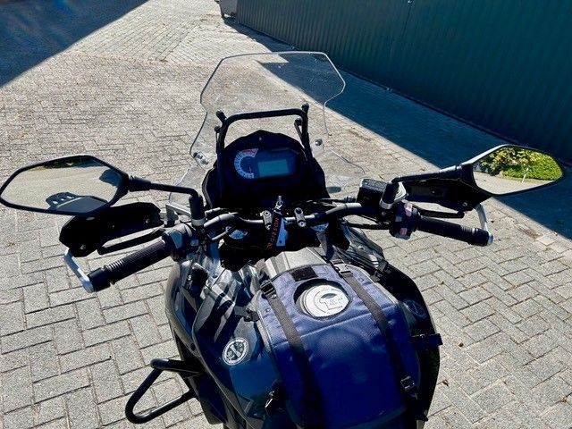 Blaues Motorrad, geparkt auf einer asphaltierten Straße neben einer blauen Mauer, gesehen vom Fahrersitz aus