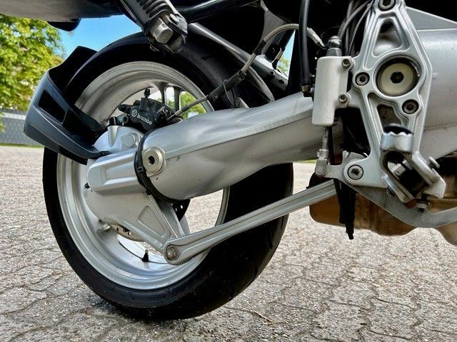 Hinterrad und Aufhängungskomponenten eines Motorrads, silber und schwarz, auf Asphalt.