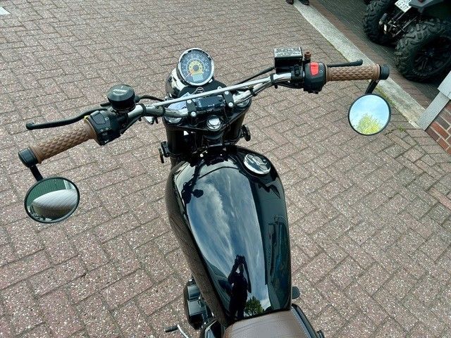 Schwarzes Motorrad, von oben auf einem Backsteinpflaster gesehen, mit sichtbaren runden Spiegeln und Lenker.