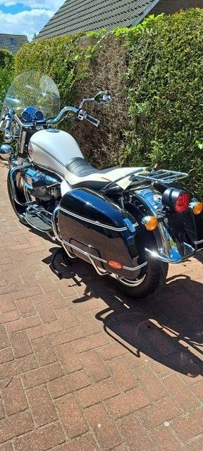 Schwarz-weißes Motorrad, geparkt auf einer Ziegelfläche mit einer grünen Hecke im Hintergrund.