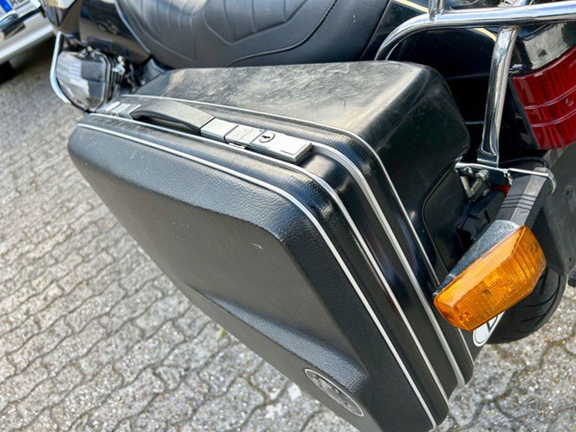 Schwarze Motorrad-Seitentasche mit silbernem Rand, neben einem gelben Blinker.
